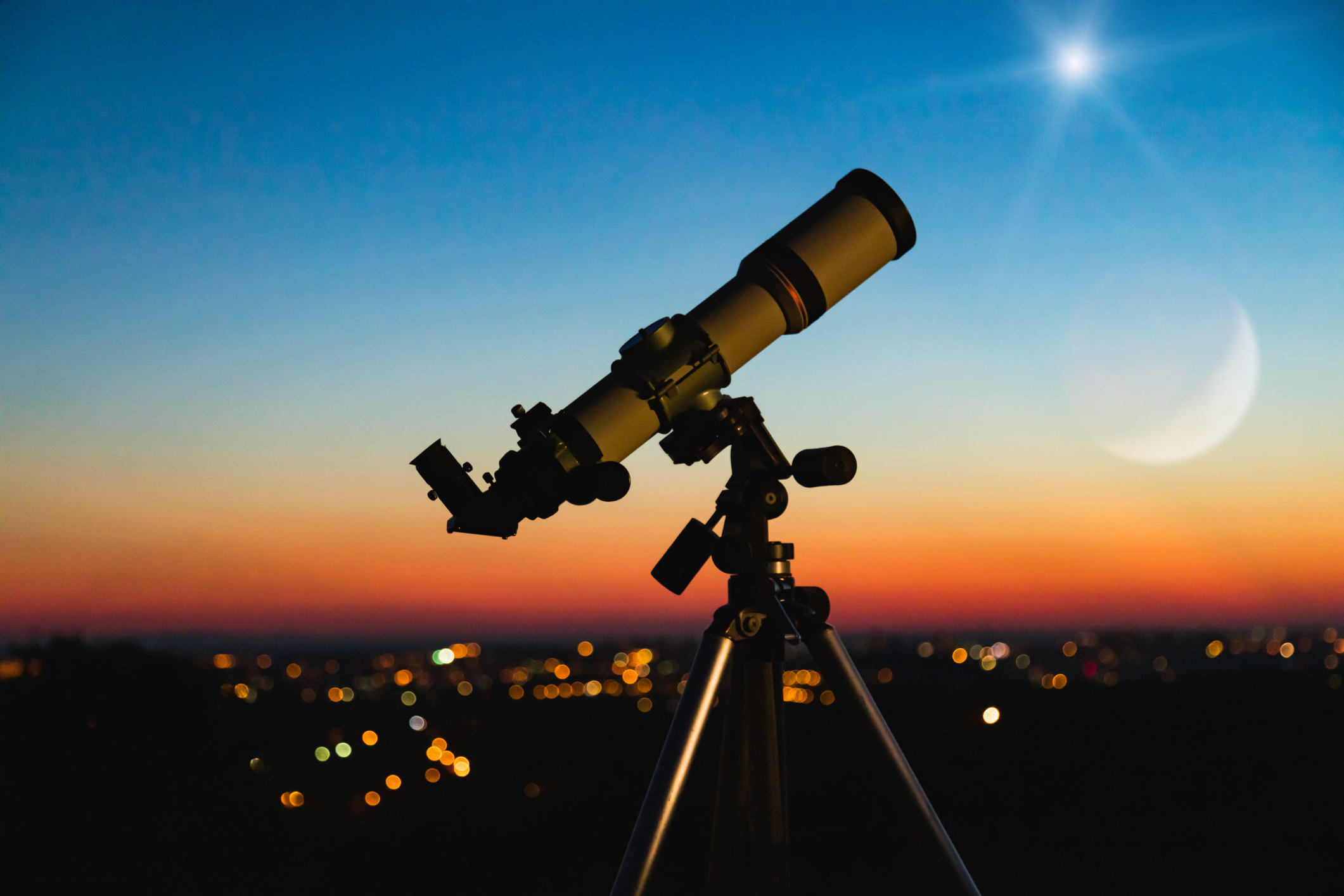 Telescope silhouette and night sky with city lights in the background.