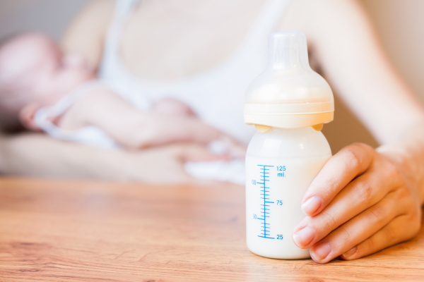 Mother holding a baby bottle with breast milk for breastfeeding at foreground, mothers breast milk is the most healthy food for newborn baby